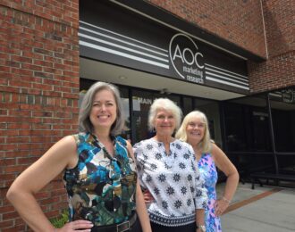 AOC Market Research's team standing in front of their new outdoor sign